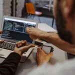 Two people coding on a laptop in an office setting