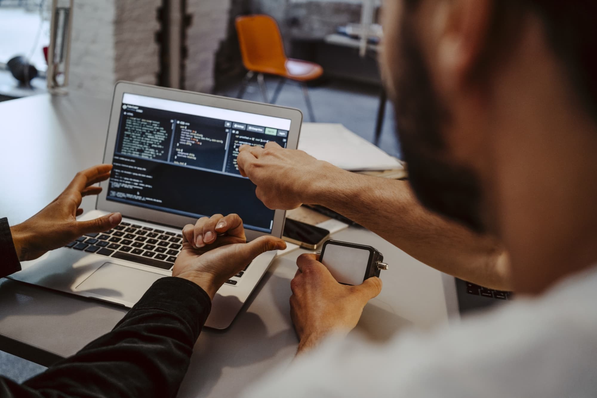 Two people coding on a laptop in an office setting